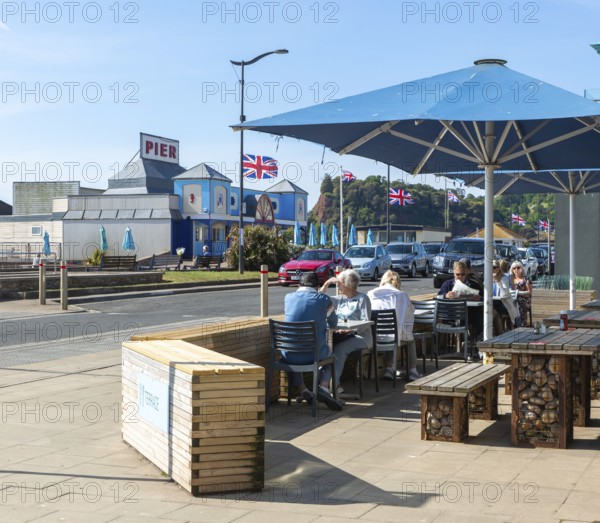 People sitting outside cafe near seafront on sunny day, Teignmouth, south Devon, England, UK