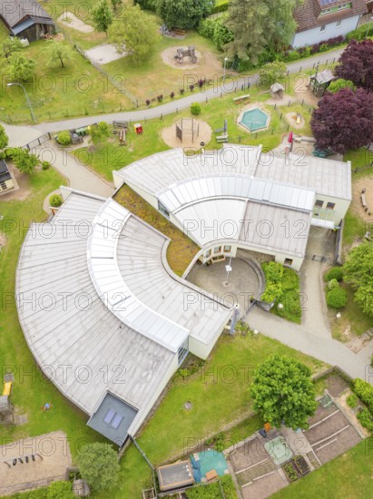 Modern architecture in a U-shaped building with surrounding greenery and playground facilities seen from the air, family party in Neubulach, district of Calw, Germany