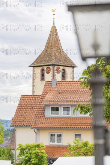 Tower of a church with clock, surrounded by buildings with red roofs and a cloudy sky, family celebration in Neubulach, district of Calw, Germany