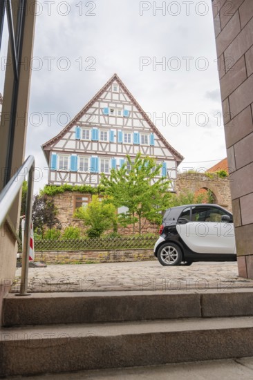 Traditional half-timbered house in the old town centre with a car in the foreground and steps, family party in Neubulach, district of Calw, Germany