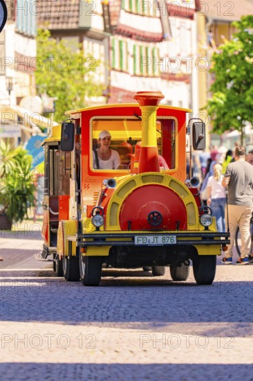 Small colourful train runs through a lively old town with cheerful people, Calw station festival, Black Forest, Germany