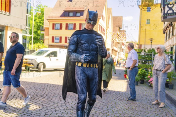 Man in Batman costume walking in a busy sunny city centre, Calw train station festival, Black Forest, Germany