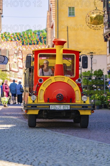 Colourful tourist train runs through a busy street full of people and decorations, Calw station festival, Black Forest, Germany