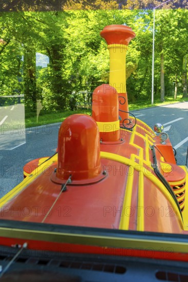 Red and yellow locomotive travelling on a green, sunny road, Calw railway station festival, Black Forest, Germany