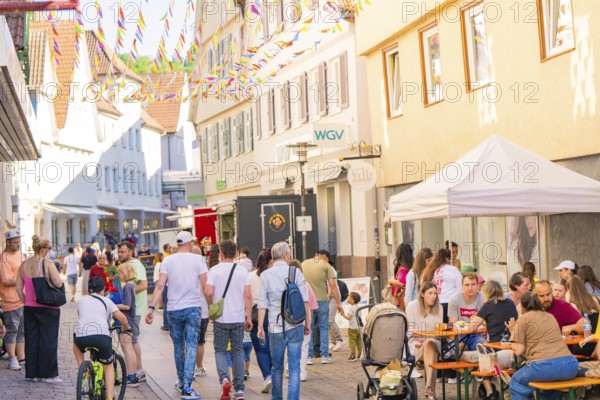 People enjoying a street festival under colourful pennants in an old town, Calw station festival, Black Forest, Germany