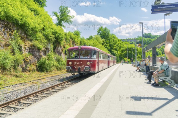 Red train stops at a sunny railway station surrounded by vegetation, Calw station festival, Black Forest, Germany