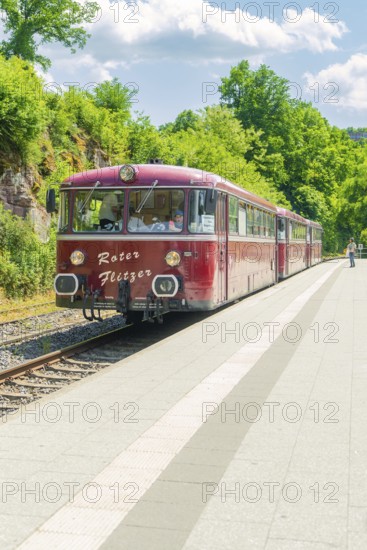 Red train stops in a rural setting on a sunny platform under a blue sky, Calw railway station festival, Black Forest, Germany