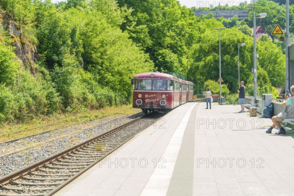 Red train approaches a sunny railway station surrounded by nature, Calw station festival, Black Forest, Germany