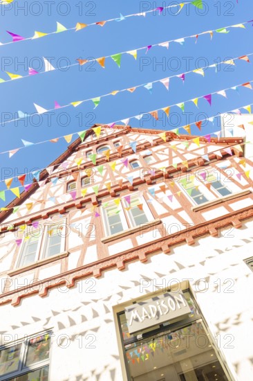 Sunlit half-timbered façade with pennants against a blue sky, Calw railway station festival, Black Forest, Germany