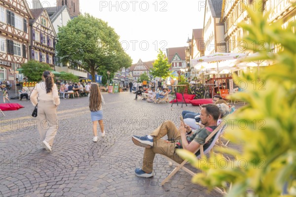 People relaxing on a lively old town square surrounded by historic buildings, Calw railway station festival, Black Forest, Germany
