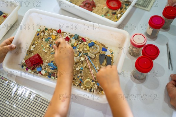 Students using tweezers collecting colorful microplastics from sand in a white plastic container during a laboratory experiment