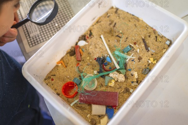 Elementary school student analyzing contaminated sand sample containing microplastics, raising awareness of plastic pollution and environmental protection