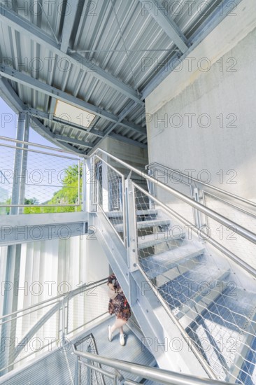 A woman on a modern metal staircase in a light-flooded interior, Zob extension with bridge construction for the new Herman Hesse railway, Calw, Black Forest, Germany