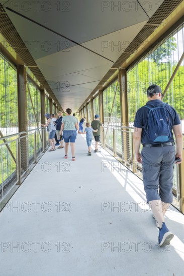 People walk over a modern glass bridge in daylight, Zob extension with bridge construction for the new Herman Hesse railway, Calw, Black Forest, Germany