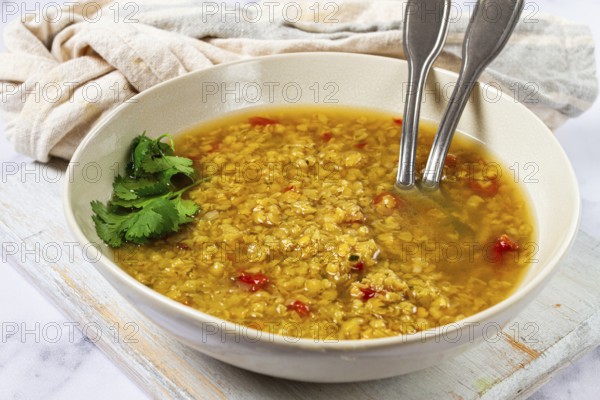 A warm lentil soup with a rich golden color is served in a rustic bowl. The soup features fresh herbs and spices, making it a comforting dish for a chilly evening