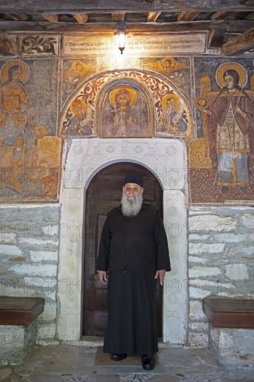 Greek Orthodox priest standing by murals from 1802, Agia Marina church, Kissos, Pelion peninsula, Thessaly, Greece