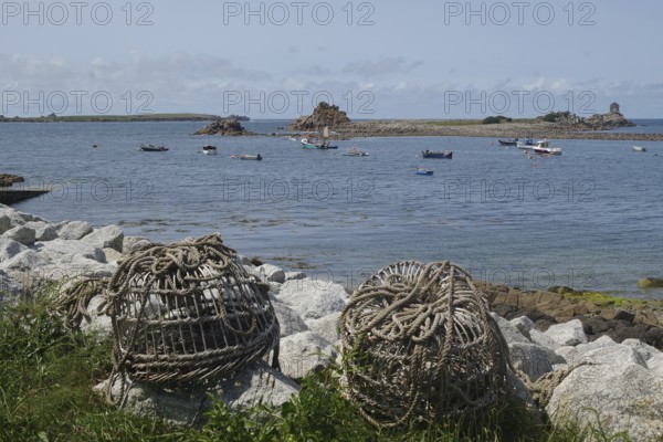 Rolled fishing baskets on a rocky coastline with boats and calm waters, St Agnes, Isles of Scilly, Cornwall, England, United Kingdom