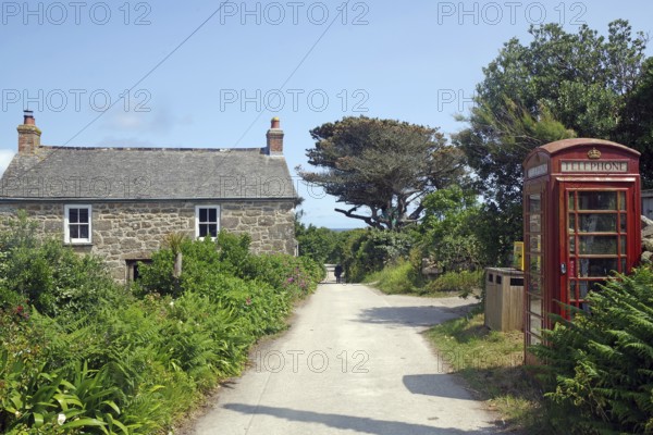 A rural scene with a stone house and red brtish telephone box along a narrow path under a blue sky, St Agnes, Isles of Scilly, Cornwall, England, United Kingdom