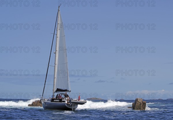 A sailing boat on the open sea, surrounded by rocks and waves, under a clear sky, St Agnes, Isles of Scilly, Cornwall, England, United Kingdom