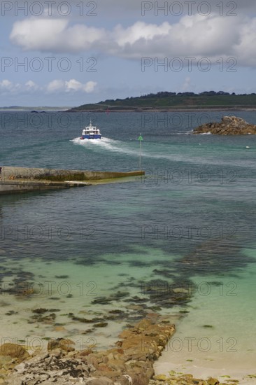 Small boat sailing through a rocky inlet on the way to the open sea, St Agnes, Isles of Scilly, Cornwall, England, United Kingdom