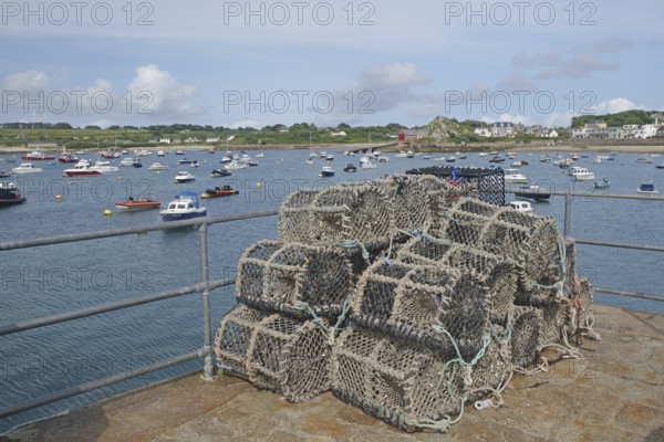 A harbour with stacked lobster pots, many boats on the water and a coastline in the background, Isles of Scilly, Cornwall, England, Great Britain