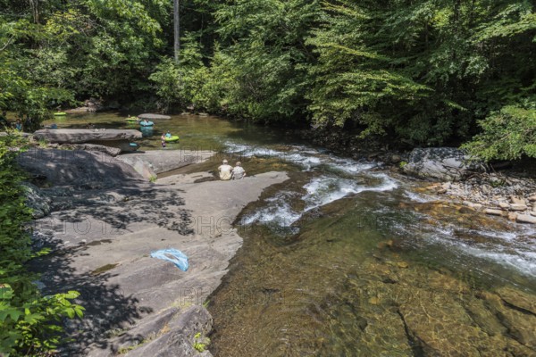 Senior couple watches children floating down the Hiawassee River on inflatable rafts near Hayesville, North Carolina, USA