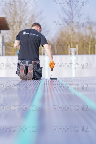 Rear view of a worker on a construction site applying strip paint with a roller, renovation of the swimming lines, Calw Stammheim outdoor pool, Calw, Black Forest, Germany
