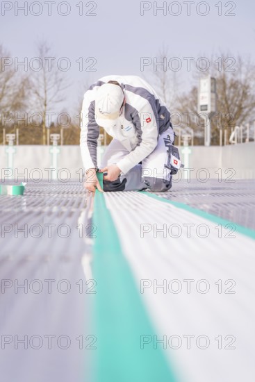 A worker kneels on the ground and precisely sticks on a green tape, renewal of the swimming lines, Calw Stammheim outdoor pool, Calw, Black Forest, Germany