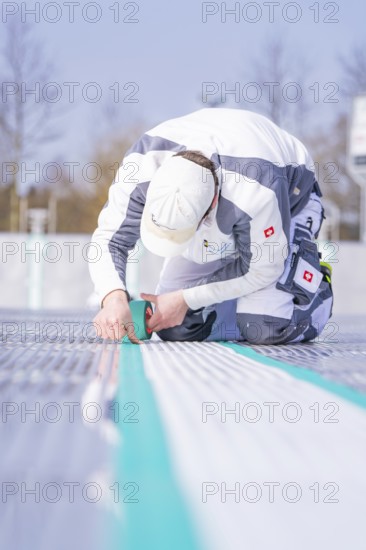 Close-up of a worker applying adhesive tape with a concentrated look on his face, renewing the swimming lines, Calw Stammheim outdoor pool, Calw, Black Forest, Germany