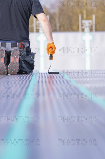 A worker kneels on the ground and applies strip paint with a paint roller, renovation of the swimming lines, Calw Stammheim outdoor pool, Calw, Black Forest, Germany