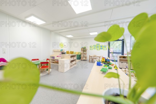 Bright classroom with play tables and a large plant in the foreground, transitional containerised daycare centre, Gechingen daycare centre, Calw district, Germany