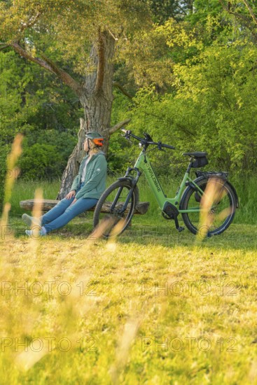 A person sits on a bench under a tree next to a bicycle in nature, e-bike excursion, Gechingen, district of Calw, Germany