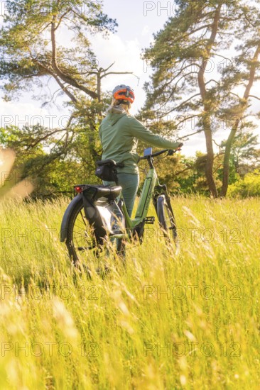 A person stands with a bicycle in the grass, surrounded by sunlight, e-bike excursion, Gechingen, district of Calw, Germany