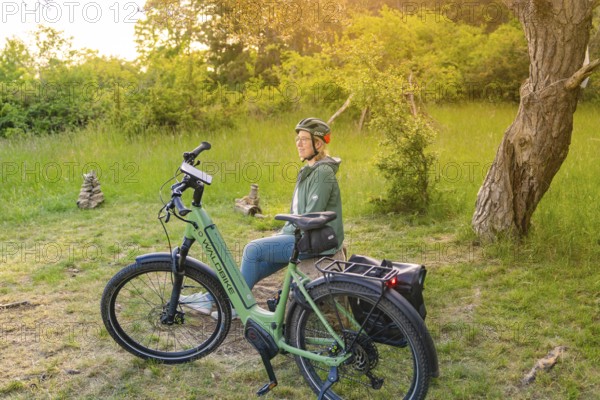 Cyclist with helmet sitting relaxed next to a bicycle in a green, summery environment, e-bike excursion, Gechingen, district of Calw, Germany