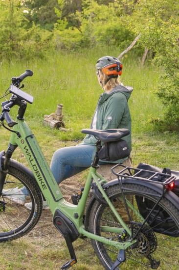 A person wearing a bicycle helmet sits on a tree stump next to a bicycle in the forest, e-bike excursion, Gechingen, district of Calw, Germany