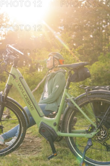 Person with helmet sitting next to a bicycle, enjoying nature in the warm sunlight, e-bike excursion, Gechingen, Landkreis Calw, Germany