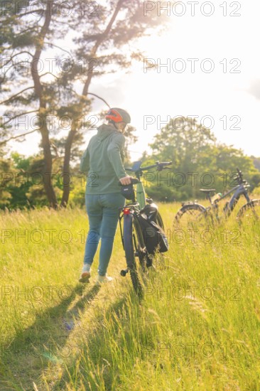 A person pushes a bicycle through high grass in a sunny field, e-bike excursion, Gechingen, district of Calw, Germany