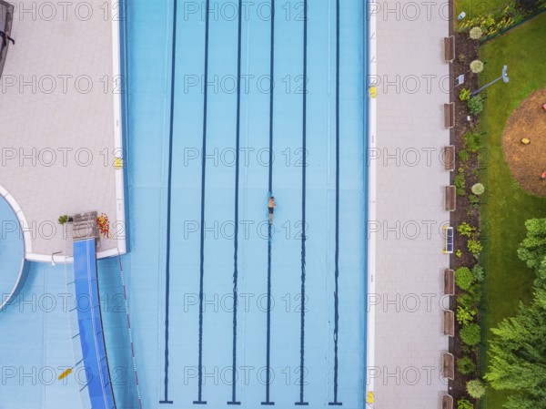 A swimmer swimming laps in a large swimming pool surrounded by green areas, Calw outdoor pool, Black Forest, Germany