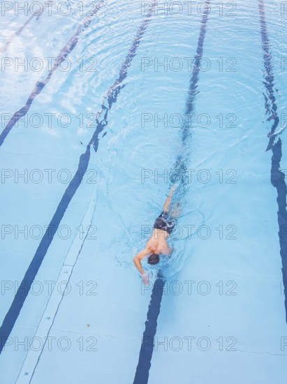 A man swims in the clear blue water of a pool along the lanes, Calw outdoor pool, Black Forest, Germany