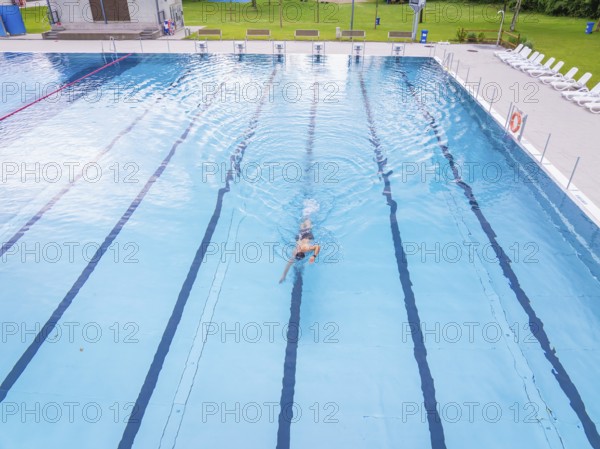 A swimmer moves alone through the lanes of a large swimming pool, Calw outdoor pool, Black Forest, Germany