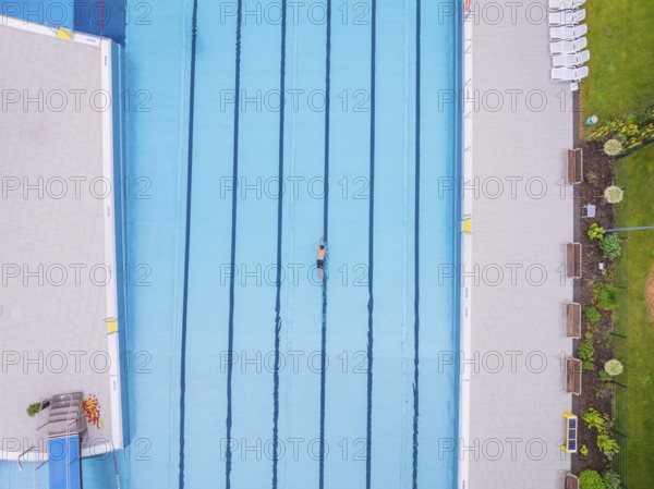 A swimmer moves in a large, empty pool next to a green meadow, Calw outdoor pool, Black Forest, Germany