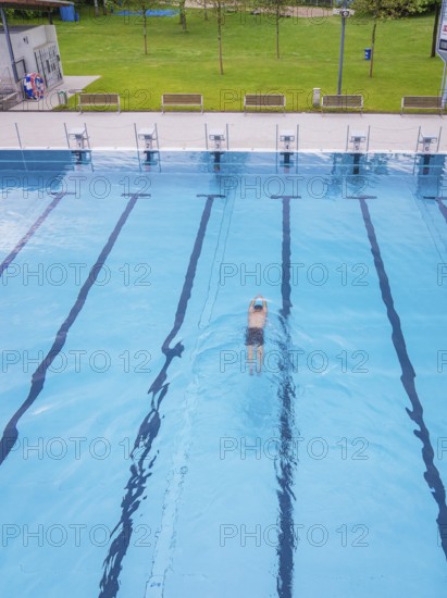 A swimmer swims in an empty, large swimming pool in sunny weather, Calw outdoor pool, Black Forest, Germany