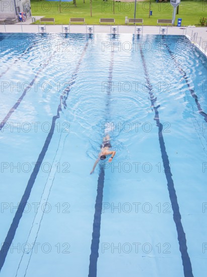 A swimmer swimming steady laps in a calm blue pool, Calw outdoor pool, Black Forest, Germany