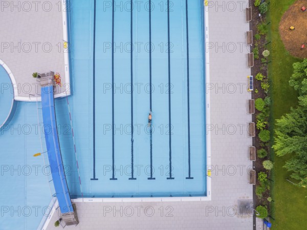 A swimmer in the large, empty pool, surrounded by paved paths and greenery, Calw outdoor pool, Black Forest, Germany