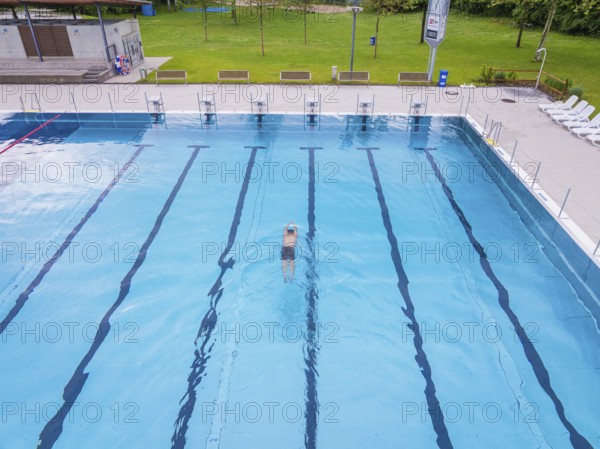 A swimmer swims in the large, clear pool on a sunny day, Calw outdoor pool, Black Forest, Germany