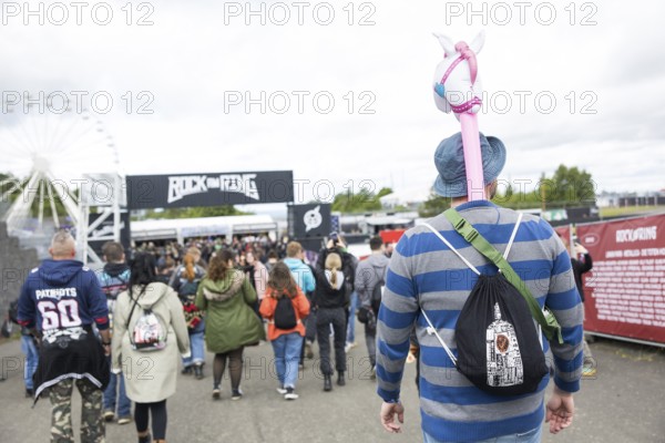 A festival visitor carries an inflatable unicorn in front of a container with the Rock am Ring logo at the Rock am Ring Festival on Friday, Nürburgring race track race track, 06/06/2025