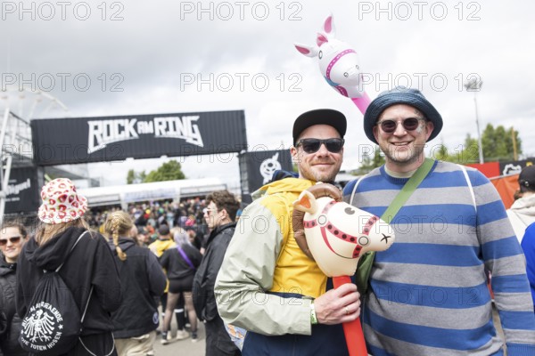 Two festival visitors with their inflatable animals Charles and Chantal in front of a container with the Rock am Ring logo at the Rock am Ring Festival on Friday, Nürburgring race track race track, 06/06/2025