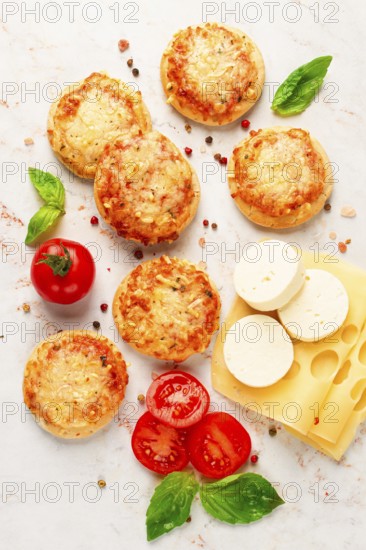 Freshly baked mini pizza on a marble table, with fresh vegetables and cheese, top view