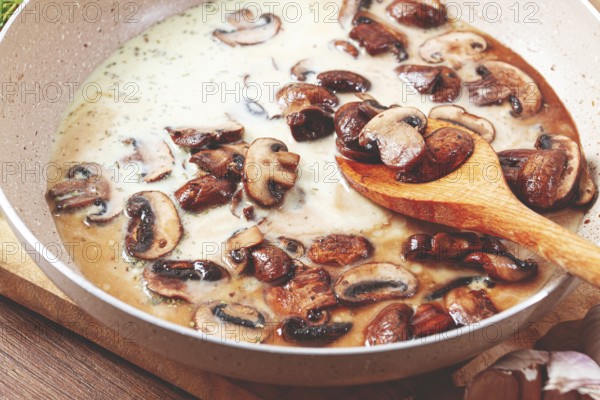 Mushrooms are cooking in a creamy sauce with garlic and herbs in a pan. Fresh thyme and garlic are on the side. The setting is a wooden table with natural colors