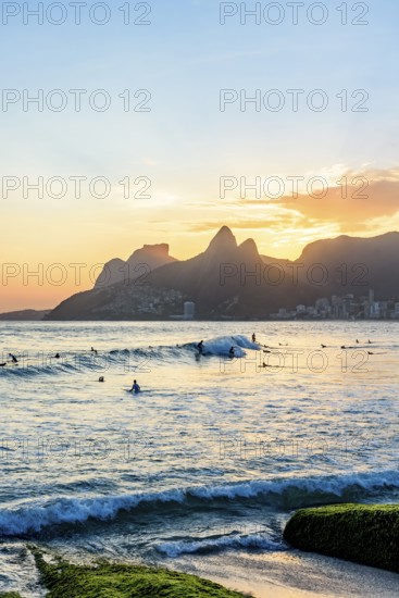 Surfing on Ipanema beach in Rio de Janeiro during sunset with the Two Brothers hill in the background, Ipanema beach, Rio de Janeiro, Rio de Janeiro, Brazil